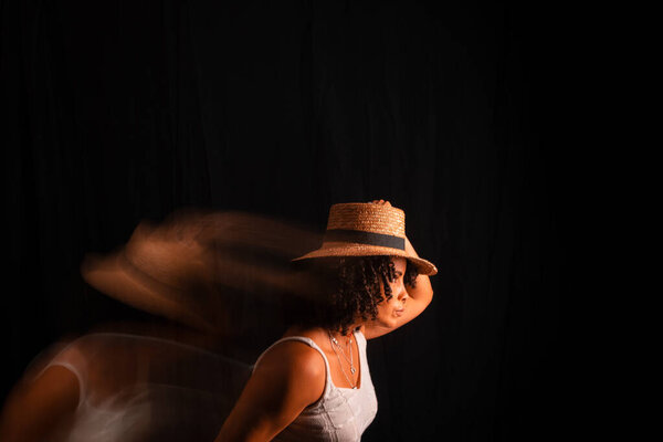 Motion blurred portrait of a woman wearing maron hat against black background.