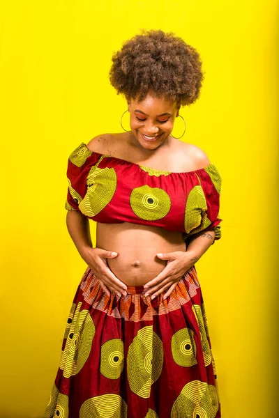 Happy pregnant woman with hand on belly. Isolated on yellow background.