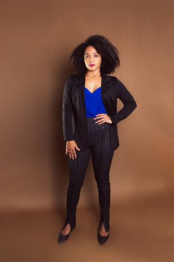 Kahverengi arka planda duran siyah ceketli bir işletmeci kadın. Stüdyo resmi.