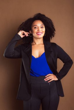 Kahverengi arka planda duran siyah ceketli bir kadın. İş kadını. Stüdyo resmi.