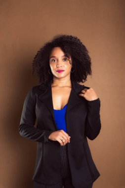 Kahverengi arka planda duran siyah ceketli bir kadın. İş kadını. Stüdyo resmi.