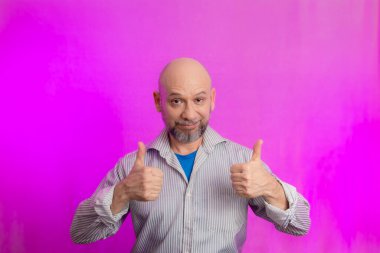 Ciddi bir adamın portresi, 50 yaşında, sakallı ve kel kafalı, el işaretleri yapan. Pembe arka planda izole edilmiş.