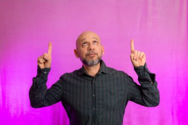 50 yaşında bir adam, komik, parmağını kaldırıyor. Pembe arka planda izole edilmiş.