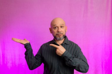 Ciddi bir adamın portresi, 50 yaşında, sakallı ve kel kafalı, el işaretleri yapan. Pembe arka planda izole edilmiş.