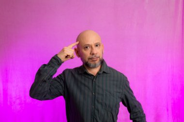 Ciddi bir adamın portresi, 50 yaşında, sakallı ve kel kafalı, el işaretleri yapan. Pembe arka planda izole edilmiş.