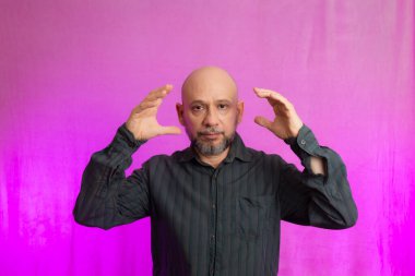 Ciddi bir adamın portresi, 50 yaşında, sakallı ve kel kafalı, el işaretleri yapan. Pembe arka planda izole edilmiş.