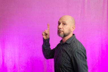 50 yaşında bir adam, komik, parmağını kaldırıyor. Pembe arka planda izole edilmiş.