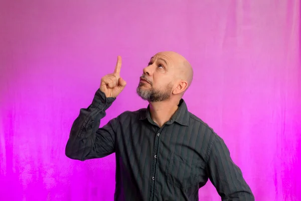 stock image 50 years old man, funny, pointing his finger up. Isolated on pink background.