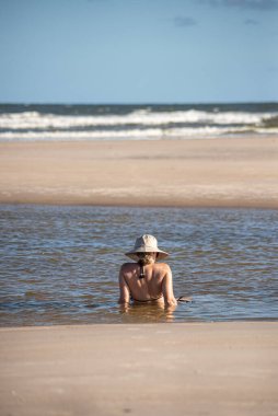 Bikini giyen ve şapkalı bir kadın denizde banyo yapıyor. Taquari, Guaibim plajı, Valenca, Bahia.