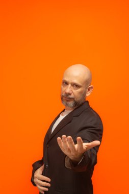 Takım elbiseli, sakallı ve kel, zarif bir adam. Turuncu arka planda izole edilmiş