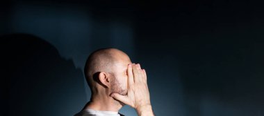 Baş ağrısı ya da migrenden muzdarip üzgün bir adam. Yüzünde acı dolu bir ifade olan stresli bir adam korkunç bir zayıflık ya da depresyon hissediyor. Koyu arkaplanda izole.