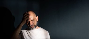 Baş ağrısı ya da migrenden muzdarip üzgün bir adam. Yüzünde acı dolu bir ifade olan stresli bir adam korkunç bir zayıflık ya da depresyon hissediyor. Koyu arkaplanda izole.