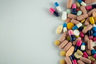 Açık gri bir yüzeye yerleştirilmiş birkaç farklı renk hapının yakın plan portresi. Tıbbi malzemeler.