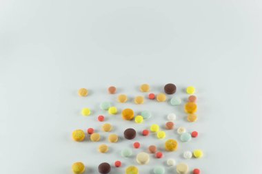 Birkaç farklı renkte hap, bazıları eski, açık gri bir yüzeye bırakılmış. Tıbbi malzemeler.