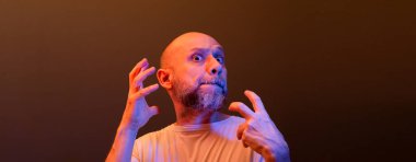 Komik el hareketleri yapan mutlu kel adam. Güç, başarı ve başarı kavramı. Koyu kırmızı arkaplanda izole.