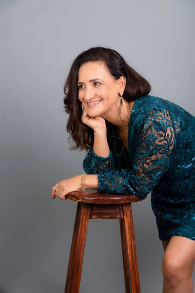 stock image Studio portrait of beautiful mature woman with elbows on wooden stool and hand on chin. Isolated on gray background.