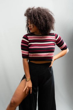 Güzel bir genç kadın, ayakta, neşeli, günlük kıyafetler içinde, kendinden oldukça emin. Açık gri arkaplanda izole.