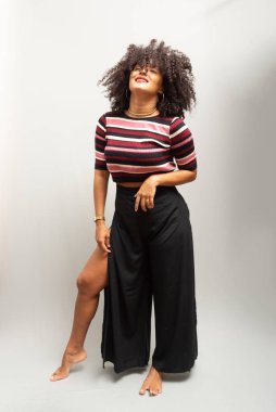 Güzel bir genç kadın, ayakta, neşeli, günlük kıyafetler içinde, kendinden oldukça emin. Açık gri arkaplanda izole.