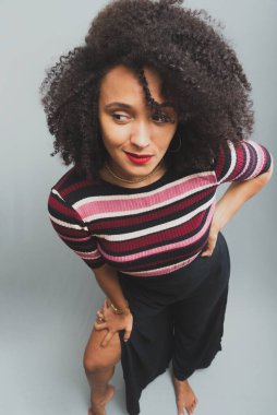 Kıvırcık saçlı ve günlük kıyafetleri olan güzel bir genç kadının portresi. Açık gri arkaplanda izole.