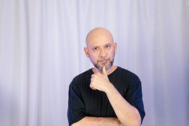 Sakallı ve kel adam elleriyle çeşitli işaretler yapıyor. Gri arkaplanda izole edilmiş.