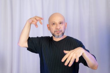 Sakallı ve kel adam elleriyle çeşitli işaretler yapıyor. Gri arkaplanda izole edilmiş.