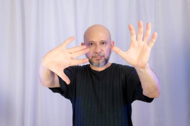 Sakallı ve kel adam elleriyle çeşitli işaretler yapıyor. Gri arkaplanda izole edilmiş.