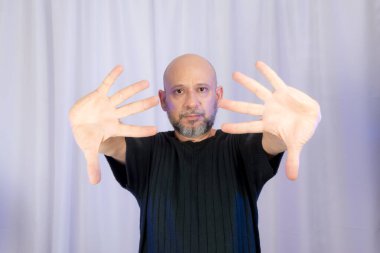 Sakallı ve kel adam elleriyle çeşitli işaretler yapıyor. Gri arkaplanda izole edilmiş.