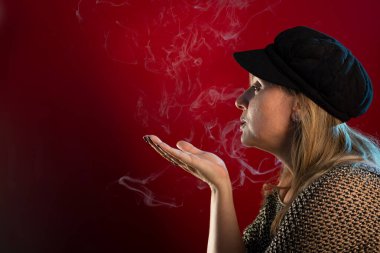 Çekici ve güzel bir kadının el kaldırılmış ve tütsü dumanı üfleyen stüdyo portresi. Kırmızı arkaplanda izole edilmiş.