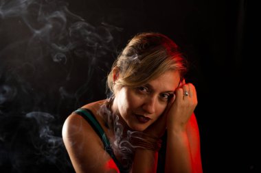 Çekici ve güzel sakin bir kadın elleri yüzünde kameraya bakıyor. Tütsü dumanı her yerde. Stüdyo portresi. Siyah bir arkaplanda izole edilmiş.