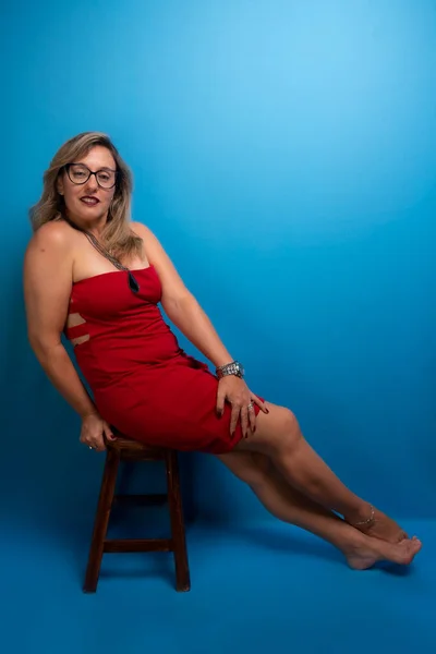 Kırmızı Elbiseli Güzel Sarışın Kadın Elleri Bacağında Oturuyor Pozitif Kişi — Stok fotoğraf