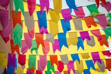 İpe asılı farklı renkte bayraklar. Sao Joao 'nun dekorasyonu. Haziran kutlaması. Sarı duvara yaslan.