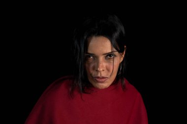 Kırmızı bir ekose kumaşa sarılı güzel, çekici esmer model kameraya bakıyor. Siyah arkaplana karşı.