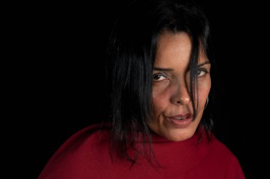 Kırmızı bir ekose kumaşa sarılı güzel, çekici esmer model kameraya bakıyor. Siyah arkaplana karşı.