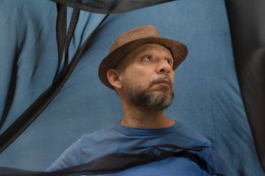 Şapkalı ve sakallı bir adam şeffaf siyah bir kumaşı manipüle ediyor. Mavi arkaplanda izole edilmiş.