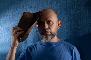 Kafasında şapka tutan sakallı adamın stüdyo portresi. Mavi arkaplanda izole.