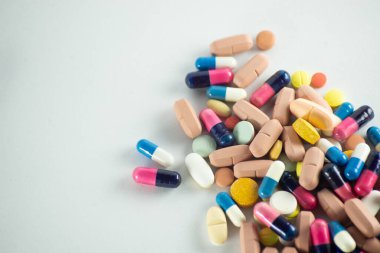 Açık gri bir yüzeye yerleştirilmiş birkaç farklı renk hapının yakın plan portresi. Tıbbi malzemeler.