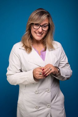 Bej ceket giymiş, gözlük takmış ve gülümseyen kendine güvenen bir kadın doktor. Pozitif kişi. Mavi arkaplanda izole