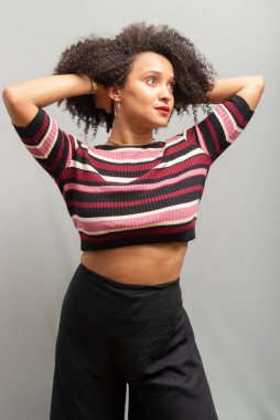 Güzel bir genç kadın, ayakta, neşeli, günlük kıyafetler içinde, kendinden oldukça emin. Açık gri arkaplanda izole.