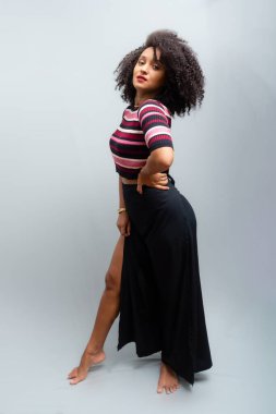 Güzel bir genç kadın, ayakta, neşeli, günlük kıyafetler içinde, kendinden oldukça emin. Açık gri arkaplanda izole.