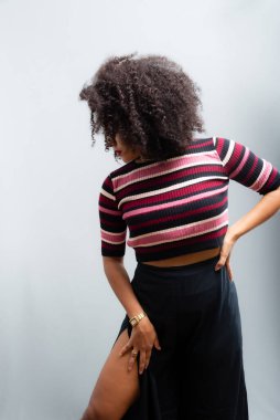 Güzel bir genç kadın, ayakta, neşeli, günlük kıyafetler içinde, kendinden oldukça emin. Açık gri arkaplanda izole.