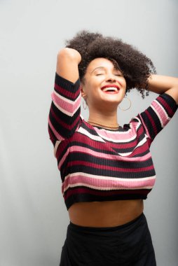 Güzel bir genç kadın, ayakta, neşeli, günlük kıyafetler içinde, kendinden oldukça emin. Açık gri arkaplanda izole.