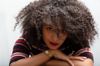 Kıvırcık saçlı, güzel, esmer bir kadının yakın plan portresi. Açık gri arkaplanda izole.