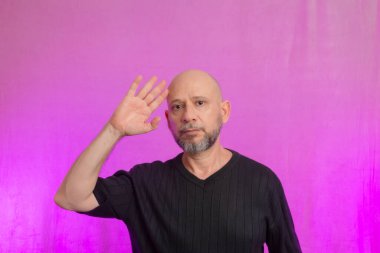 Sakallı ve kel bir adamın portresi. Ellerle tabela yapıyor. Pembe arka planda izole edilmiş.