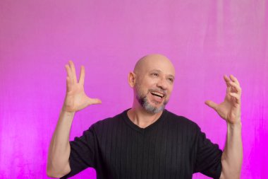 Sakallı ve kel adam elleriyle çeşitli işaretler yapıyor. Pembe arka planda izole edilmiş.