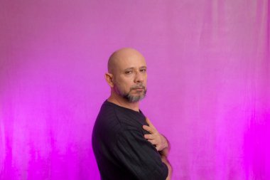 50 yaşında sakallı ve kel kafalı ciddi bir adamın portresi. Pembe arka planda izole edilmiş.