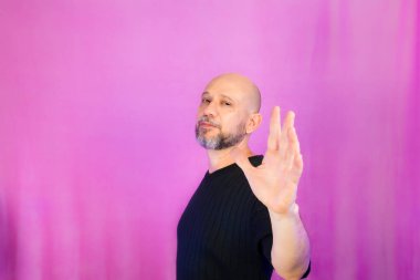 Sakallı ve kel adam elleriyle çeşitli işaretler yapıyor. Pembe arka planda izole edilmiş.