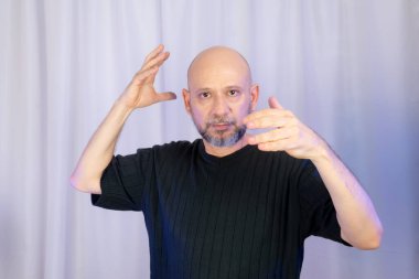 Sakallı ve kel adam elleriyle çeşitli işaretler yapıyor. Gri arkaplanda izole edilmiş.