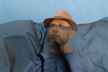 Şapkalı ve sakallı bir adam şeffaf siyah bir kumaşı manipüle ediyor. Mavi arkaplanda izole edilmiş.