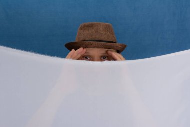 Beyaz renkli kumaşın arkasında şapka takan bir adam. Mavi arkaplanda izole edilmiş.