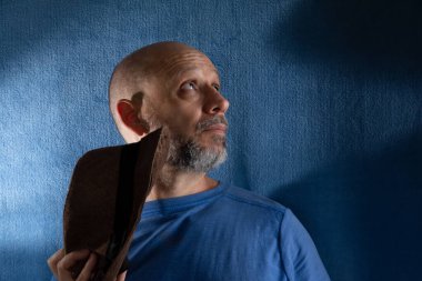 Kafasında şapka tutan sakallı adamın stüdyo portresi. Mavi arkaplanda izole.